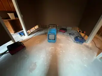 Commercial dehumidifier and air movers running on bare concrete basement floor with exposed lower wall framing after drywall removal — Marietta, GA