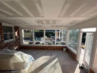 Sunroom during storm restoration with freshly mudded drywall ceiling, exposed brick walls, and bare concrete subfloor — Marietta, GA